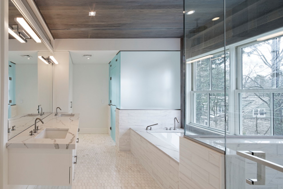 Large classic ensuite bathroom in New York with flat-panel cabinets, white cabinets, white tiles, stone slabs, white walls, mosaic tile flooring, a submerged sink, a freestanding bath, a walk-in shower, a two-piece toilet, marble worktops, white floors and a hinged door.