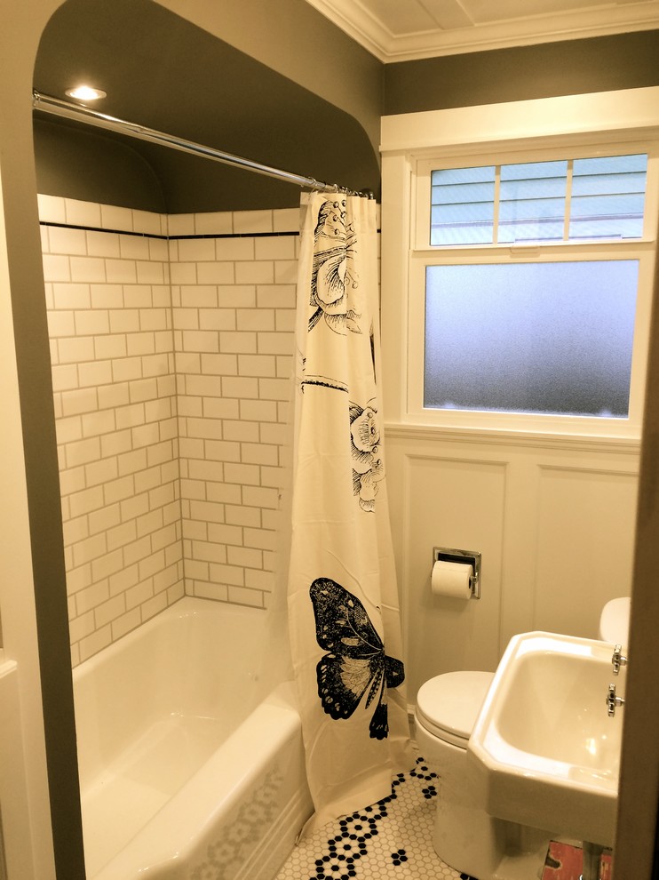 Klassisk inredning av ett litet badrum, med ett väggmonterat handfat, luckor med infälld panel, vita skåp, ett badkar i en alkov, en dusch/badkar-kombination, en toalettstol med separat cisternkåpa, vit kakel, tunnelbanekakel, grå väggar och mosaikgolv