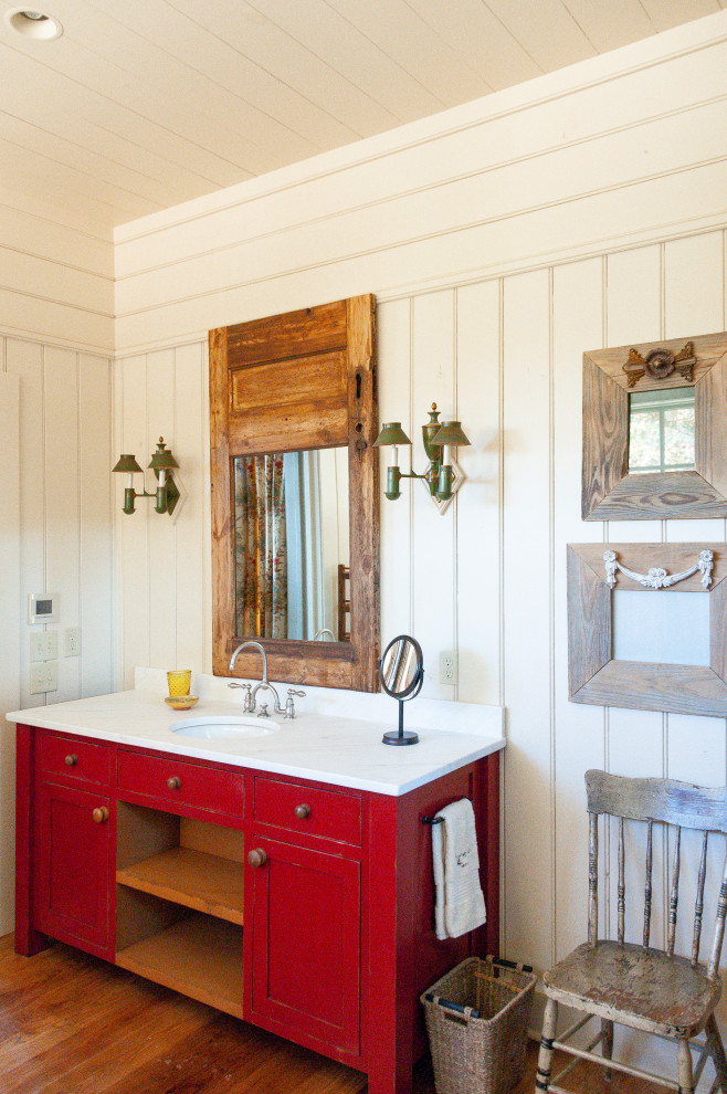 Cette image montre une salle de bain principale chalet de taille moyenne avec un placard en trompe-l'oeil, des portes de placard rouges, un mur blanc, parquet foncé, un plan de toilette en marbre, un sol marron et un plan de toilette blanc.
