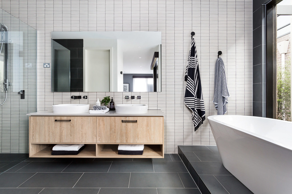 Foto de cuarto de baño contemporáneo con bañera exenta, suelo gris, armarios con paneles lisos, puertas de armario de madera clara, baldosas y/o azulejos blancos, lavabo sobreencimera y encimeras grises