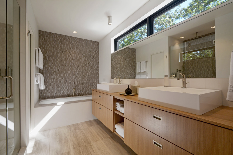 На фото: главная ванная комната в современном стиле с плоскими фасадами, фасадами цвета дерева среднего тона, полновстраиваемой ванной, коричневой плиткой, серой плиткой, белыми стенами и настольной раковиной с
