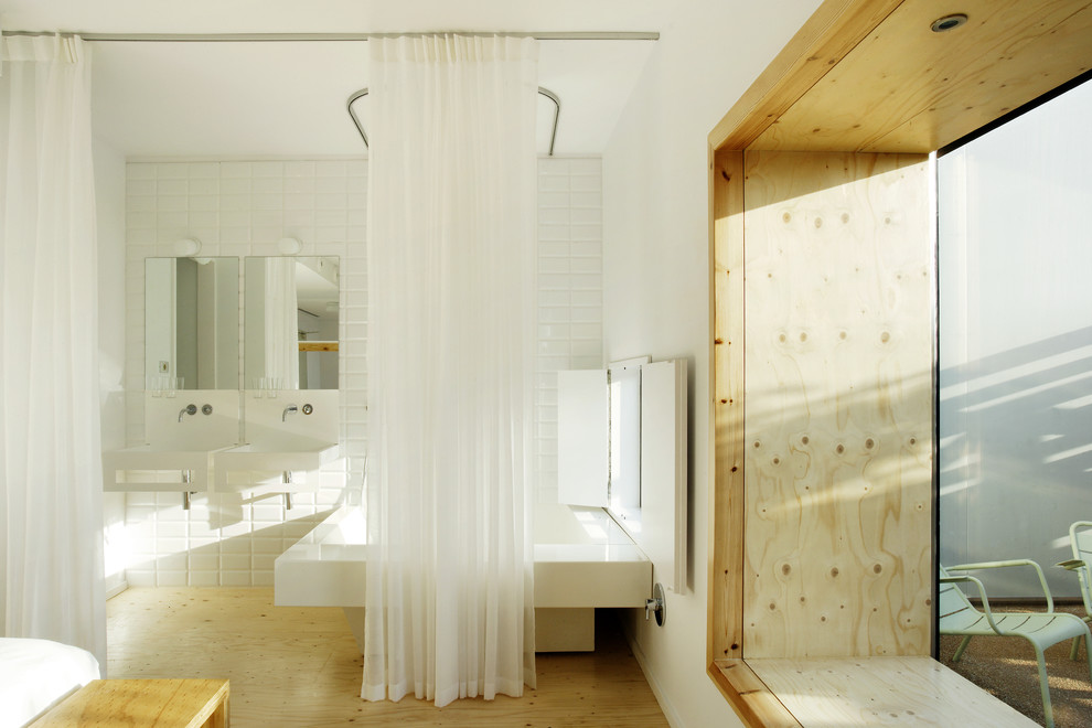 This is an example of a large contemporary ensuite bathroom in Barcelona with an alcove bath, a shower/bath combination, white tiles, metro tiles, white walls, light hardwood flooring and a wall-mounted sink.