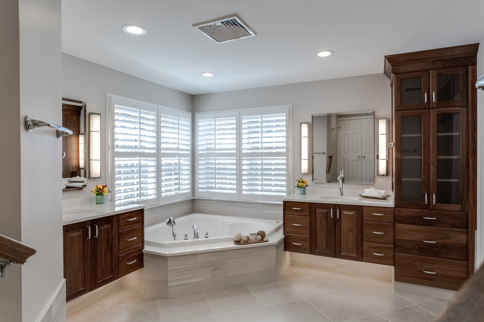 Photo of a large traditional ensuite bathroom in DC Metro with raised-panel cabinets, dark wood cabinets, a corner bath, a walk-in shower, a one-piece toilet, grey walls, ceramic flooring, a submerged sink, quartz worktops, grey floors, a sliding door, white worktops, grey tiles and porcelain tiles.