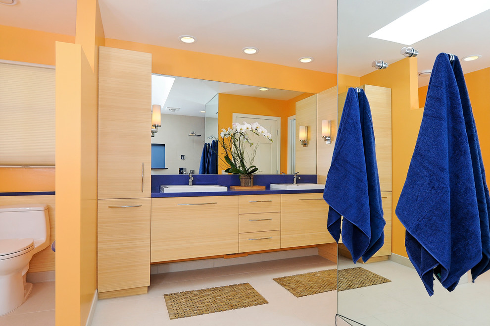 Aménagement d'une salle de bain contemporaine en bois clair avec un lavabo posé, un placard à porte plane, un mur orange et un plan de toilette bleu.