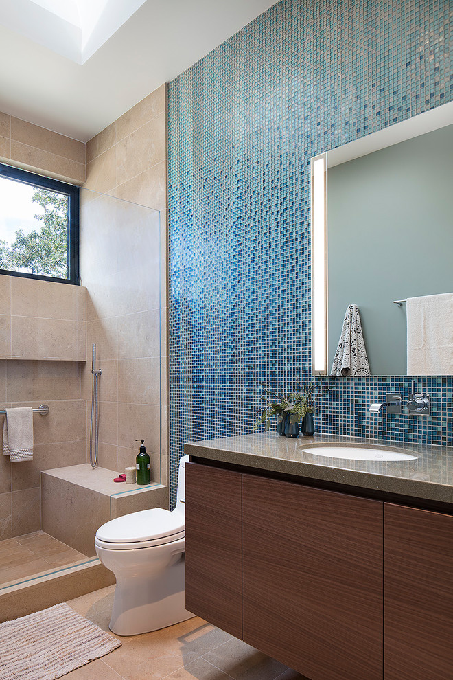 На фото: детская ванная комната среднего размера в современном стиле с плоскими фасадами, темными деревянными фасадами, душем в нише, унитазом-моноблоком, синей плиткой, стеклянной плиткой, полом из известняка, врезной раковиной, столешницей из искусственного кварца, бежевым полом, коричневой столешницей и зеркалом с подсветкой