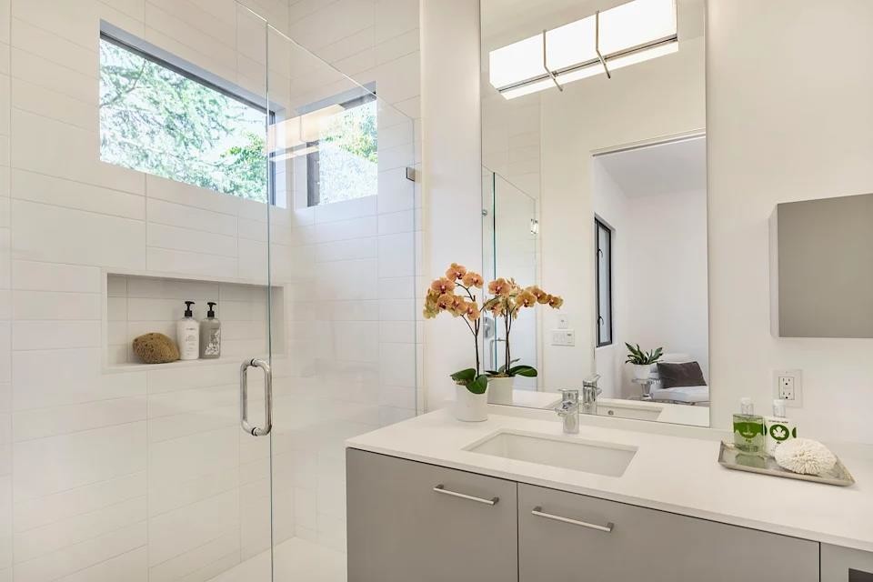 На фото: ванная комната в стиле модернизм с плоскими фасадами, серыми фасадами, душем в нише, белой плиткой, плиткой кабанчик, белыми стенами, врезной раковиной, душем с распашными дверями и белой столешницей