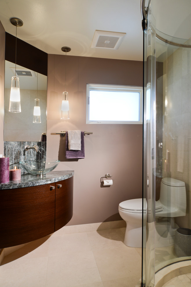 Modelo de cuarto de baño actual con lavabo sobreencimera, armarios con paneles lisos, puertas de armario de madera oscura, encimera de granito, ducha esquinera y sanitario de una pieza