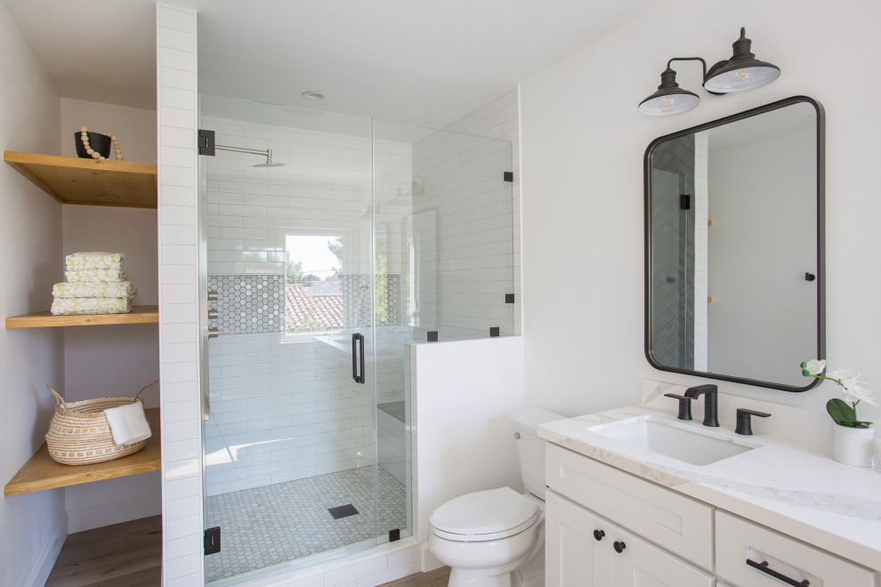На фото: главная ванная комната среднего размера в современном стиле с фасадами с декоративным кантом, белыми фасадами, угловым душем, унитазом-моноблоком, коричневой плиткой, плиткой кабанчик, белыми стенами, полом из ламината, врезной раковиной, столешницей из искусственного кварца, коричневым полом, душем с распашными дверями, белой столешницей, сиденьем для душа, тумбой под две раковины и встроенной тумбой с