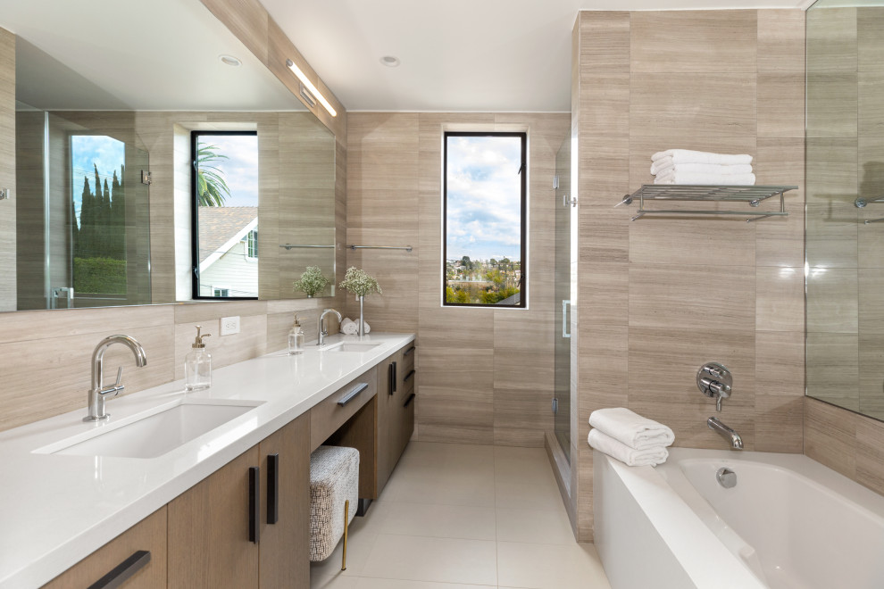 Inspiration for a contemporary ensuite bathroom in Los Angeles with flat-panel cabinets, medium wood cabinets, an alcove bath, beige tiles, stone tiles, beige walls, porcelain flooring, a submerged sink, engineered stone worktops, white floors, white worktops, double sinks and a built in vanity unit.