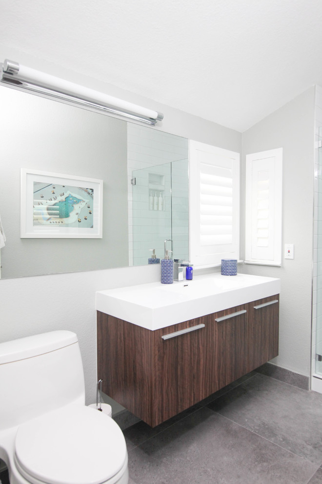 Modern inredning av ett badrum för barn, med släta luckor, skåp i mellenmörkt trä, ett badkar i en alkov, en dusch/badkar-kombination, vit kakel, grå väggar, klinkergolv i porslin och grått golv
