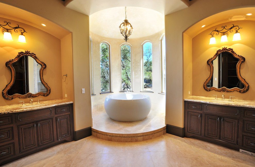 Large mediterranean ensuite bathroom in Sacramento with raised-panel cabinets, dark wood cabinets, a freestanding bath, beige walls, travertine flooring, granite worktops, a submerged sink, beige floors, an alcove shower, beige tiles, porcelain tiles, a hinged door and a two-piece toilet.