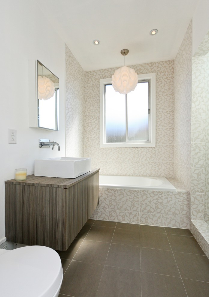 Cette image montre une salle de bain design avec une vasque, un placard à porte plane, des portes de placard grises, un plan de toilette en bois, une baignoire posée et un carrelage multicolore.