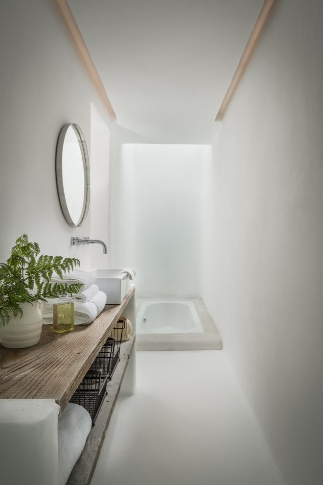 Cette photo montre une salle d'eau nature en bois brun avec un placard sans porte, une baignoire posée, un mur blanc, une vasque, un plan de toilette en bois, un sol blanc et un plan de toilette marron.