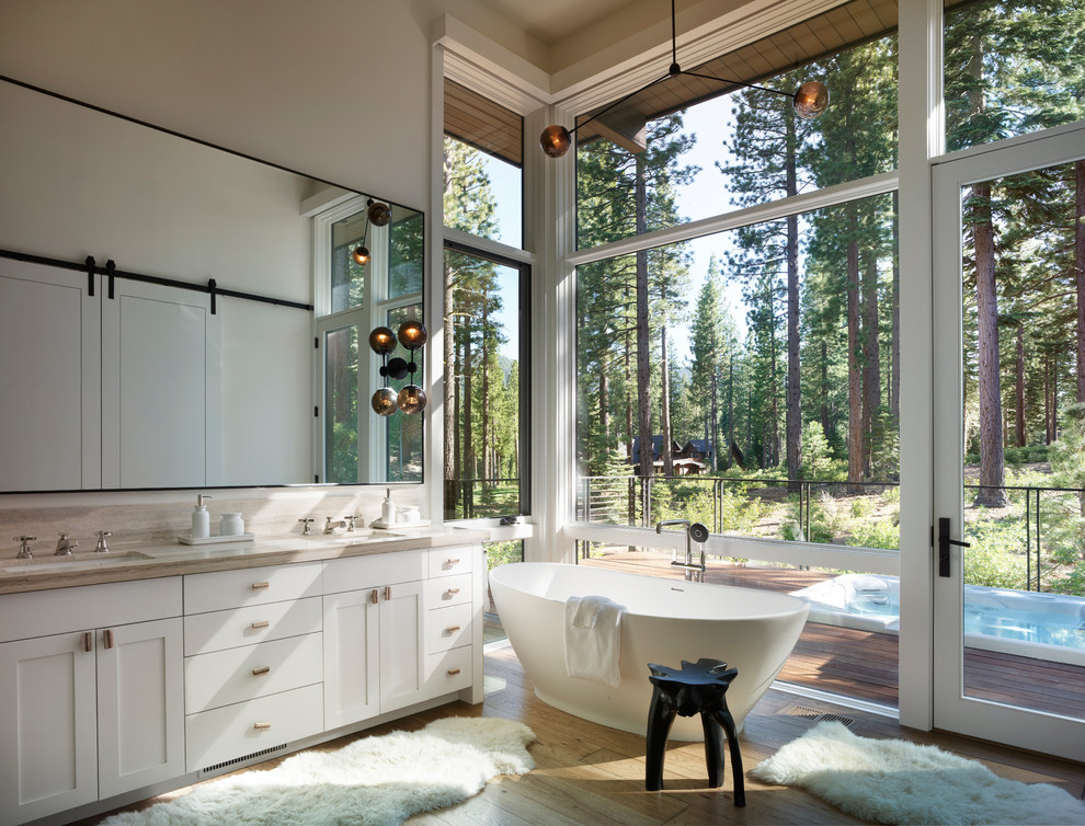 Inredning av ett modernt beige beige en-suite badrum, med skåp i shakerstil, vita skåp, ett fristående badkar, grå väggar, ljust trägolv, ett undermonterad handfat och beiget golv