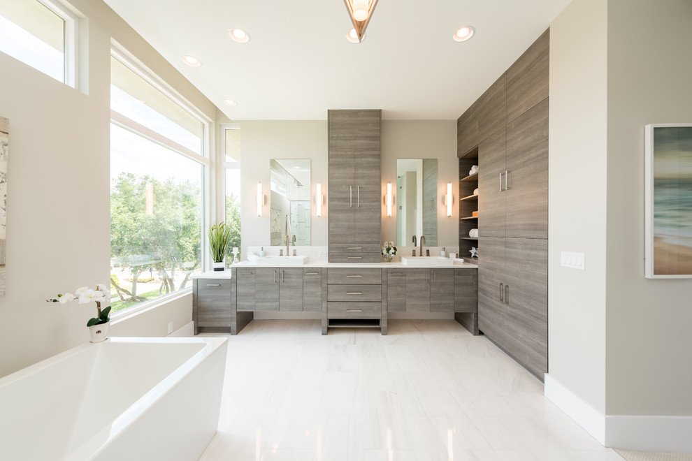 На фото: главная ванная комната в современном стиле с плоскими фасадами, фасадами цвета дерева среднего тона, отдельно стоящей ванной, бежевыми стенами, настольной раковиной, белым полом и белой столешницей с