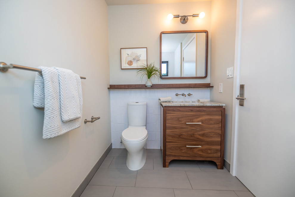 Пример оригинального дизайна: маленькая детская ванная комната в стиле ретро с плоскими фасадами, темными деревянными фасадами, полновстраиваемой ванной, душем над ванной, раздельным унитазом, серой плиткой, керамической плиткой, белыми стенами, полом из керамогранита, врезной раковиной, столешницей из искусственного кварца, серым полом, душем с распашными дверями и бежевой столешницей для на участке и в саду
