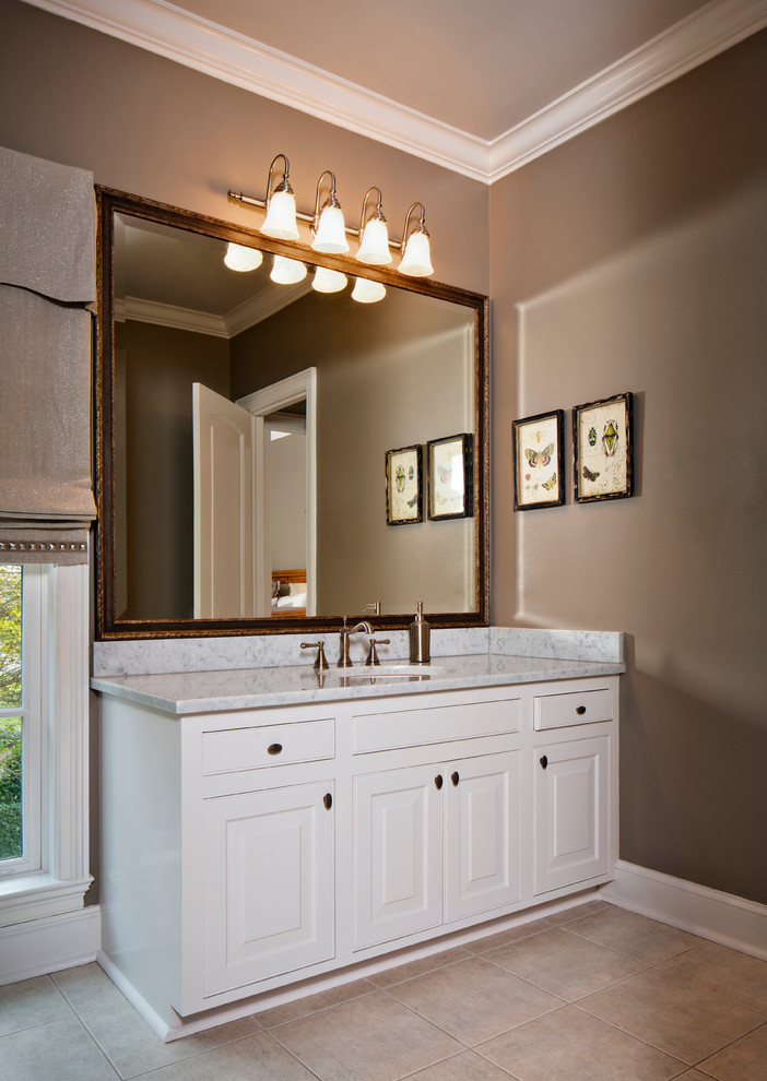 Inredning av ett klassiskt mellanstort badrum, med ett undermonterad handfat, luckor med profilerade fronter, vita skåp, marmorbänkskiva, en dusch/badkar-kombination, beige kakel, keramikplattor, bruna väggar och klinkergolv i keramik