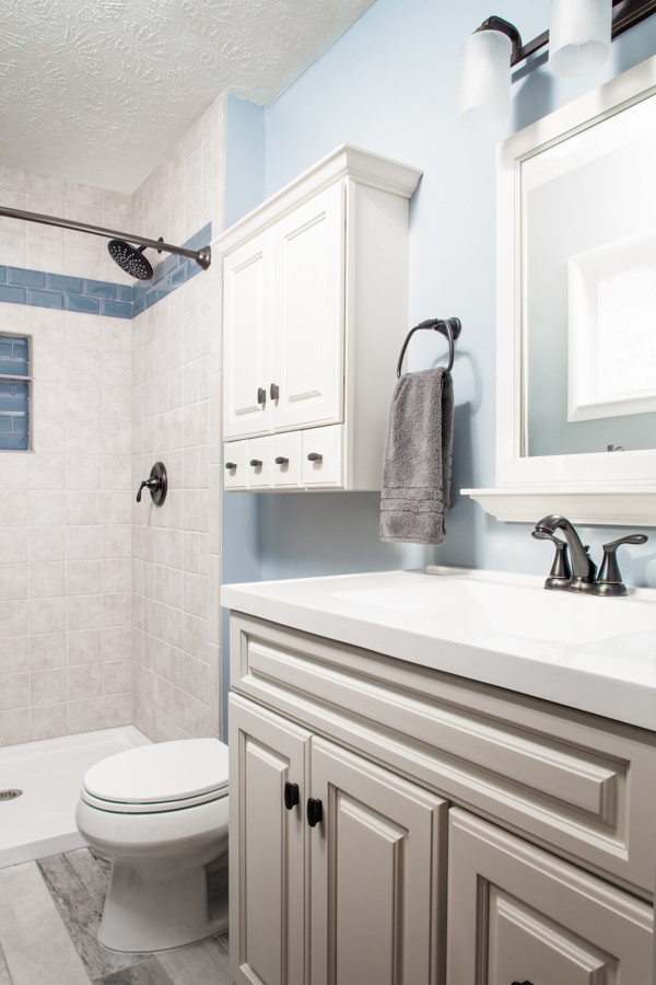 Kleines Klassisches Duschbad mit Schrankfronten im Shaker-Stil, beigen Schränken, Duschnische, Wandtoilette mit Spülkasten, beigen Fliesen, Keramikfliesen, blauer Wandfarbe, Keramikboden, integriertem Waschbecken, buntem Boden und Duschvorhang-Duschabtrennung in Omaha