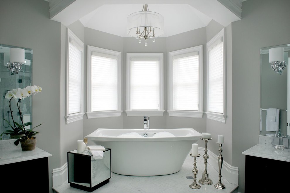 Идея дизайна: большая ванная комната в стиле неоклассика (современная классика) с черными фасадами, отдельно стоящей ванной, серыми стенами, мраморным полом и мраморной столешницей