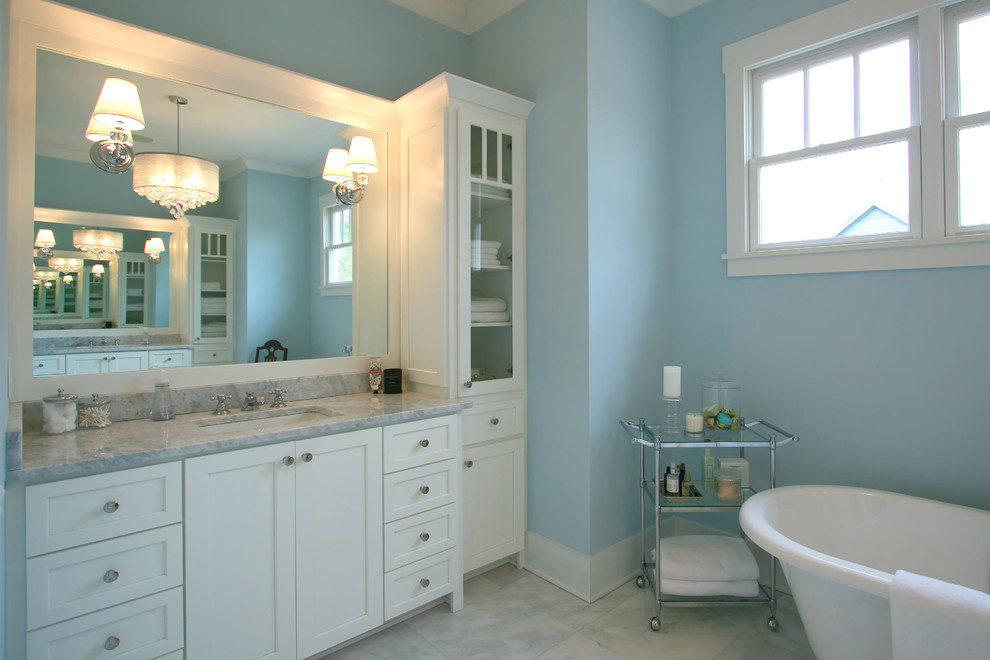 This is an example of a traditional ensuite bathroom in Charlotte with a submerged sink, flat-panel cabinets, white cabinets, marble worktops, a freestanding bath, a corner shower, blue walls and marble flooring.