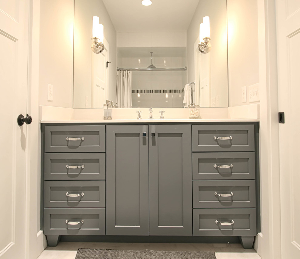 Cette photo montre une salle de bain chic avec un placard à porte plane, des portes de placard grises, un plan de toilette en marbre et un combiné douche/baignoire.