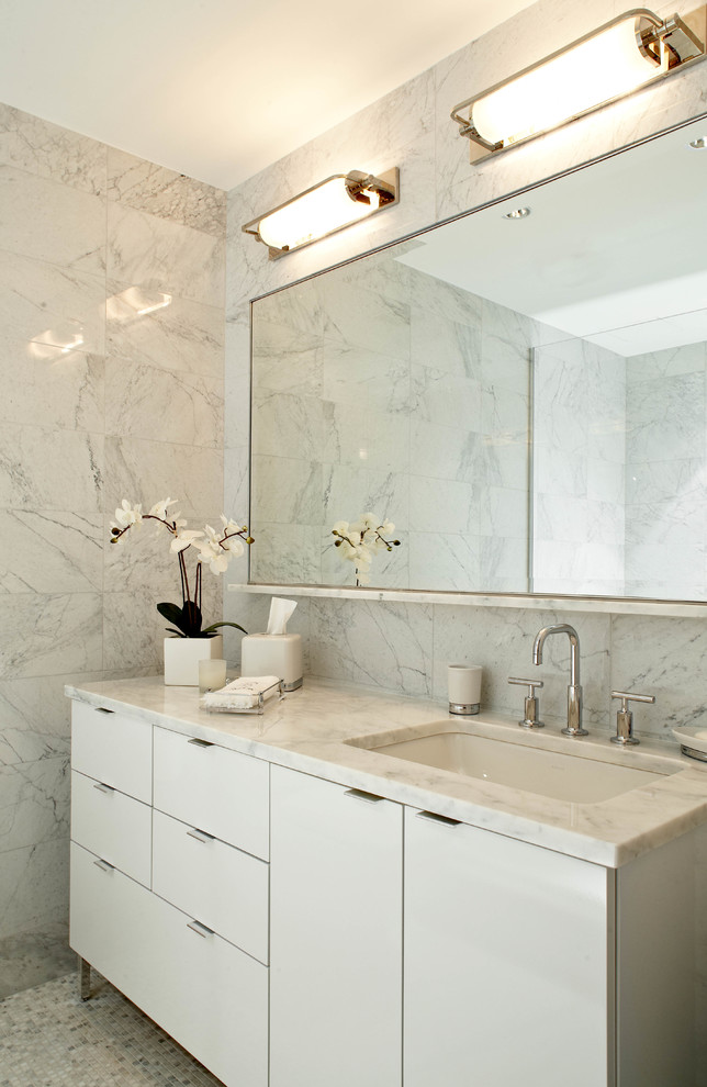 Modelo de cuarto de baño actual con lavabo bajoencimera, armarios con paneles lisos, puertas de armario blancas, baldosas y/o azulejos blancos y suelo con mosaicos de baldosas