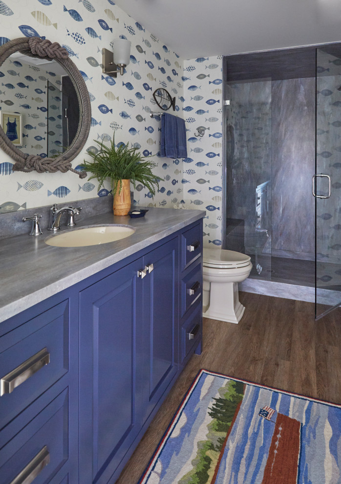 Inspiration for a mid-sized craftsman kids' laminate floor and brown floor alcove shower remodel in Milwaukee with raised-panel cabinets, blue cabinets, a two-piece toilet, multicolored walls, an undermount sink, solid surface countertops, a hinged shower door and blue countertops