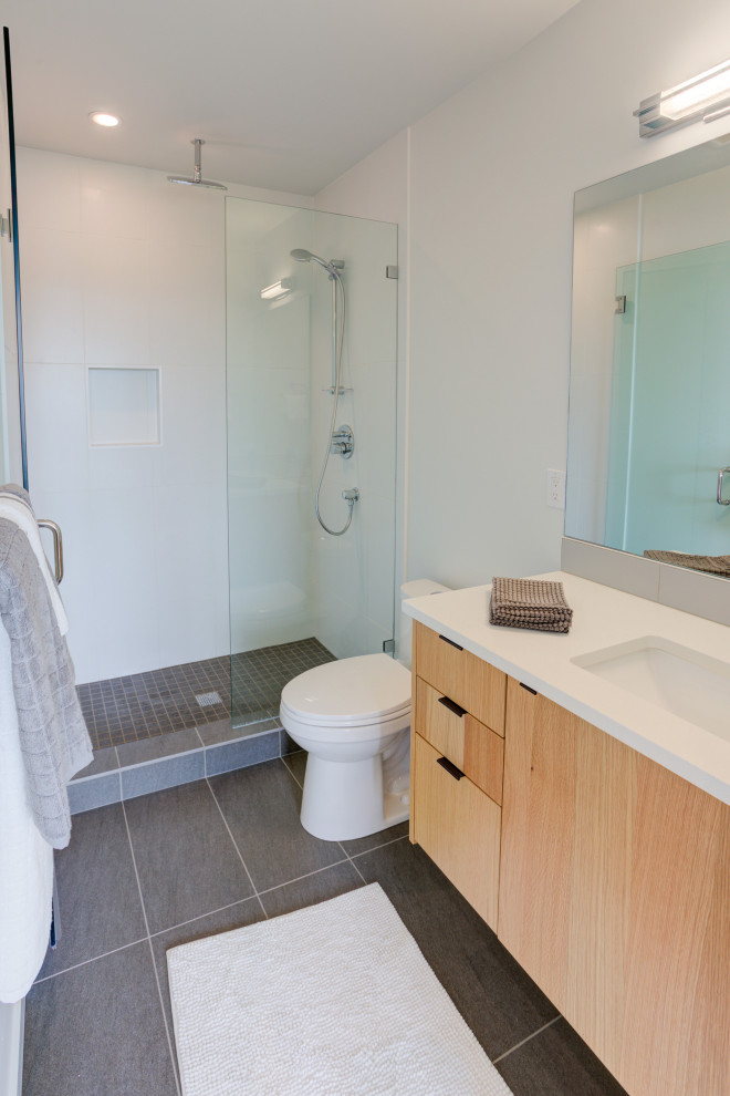Exemple d'une petite salle de bain moderne en bois clair avec un placard à porte plane, WC à poser, un carrelage blanc, un mur blanc, un sol en carrelage de céramique, un lavabo encastré, un plan de toilette en quartz modifié, un sol gris, une cabine de douche à porte battante et un plan de toilette blanc.