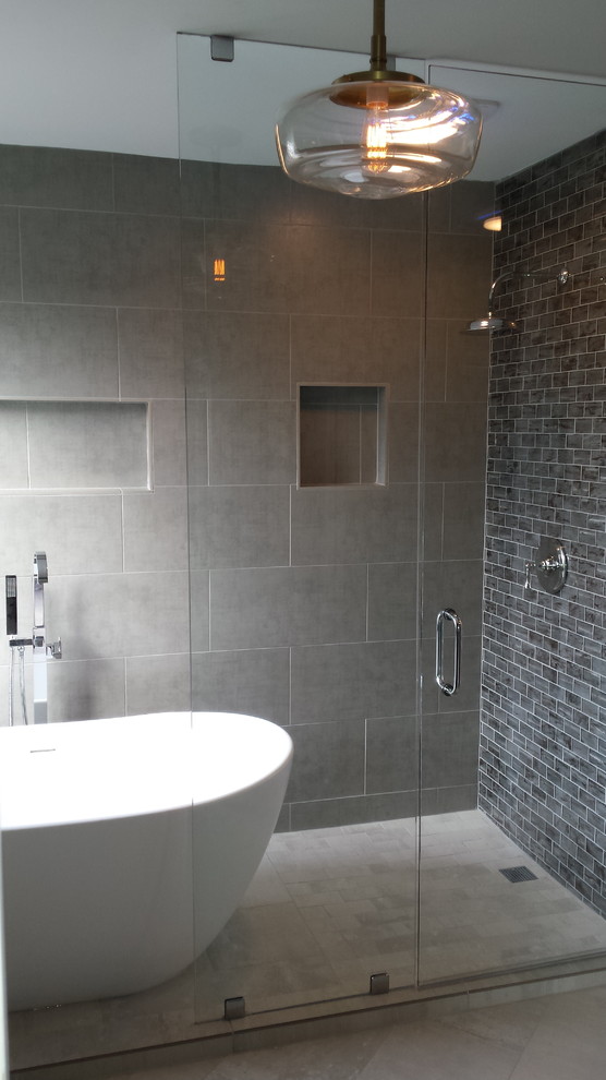 На фото: большая главная ванная комната в стиле модернизм с отдельно стоящей ванной, открытым душем, серой плиткой, керамогранитной плиткой, серыми стенами, полом из керамогранита, серым полом и душем с распашными дверями