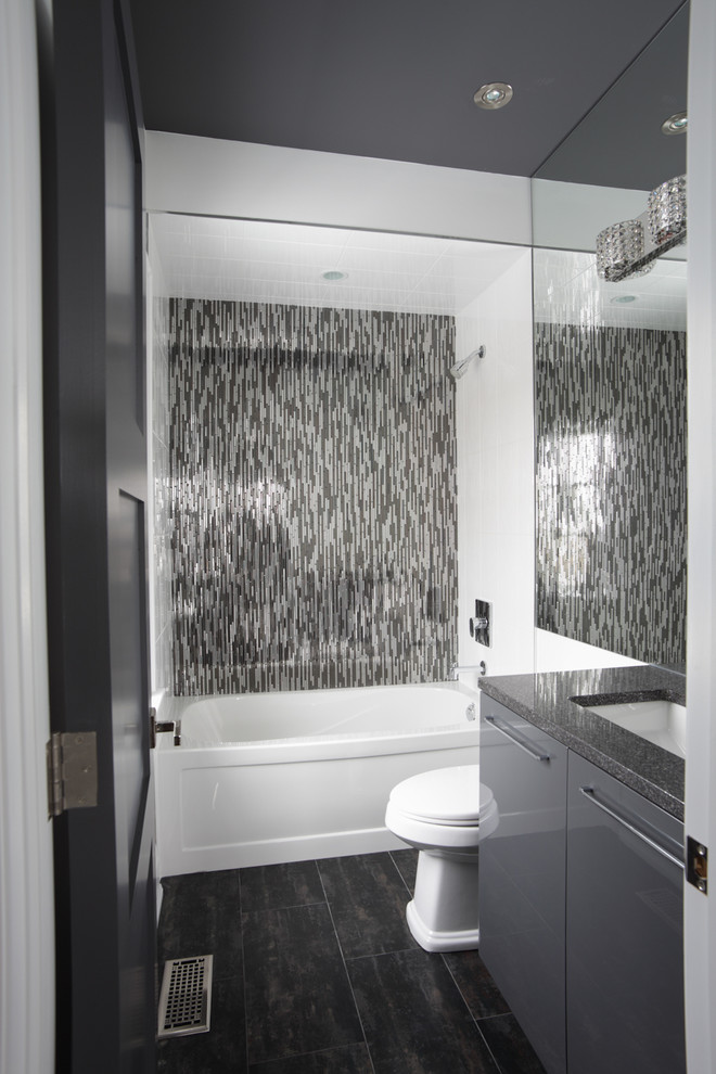 Inspiration för ett litet funkis grå grått badrum med dusch, med grå skåp, ett badkar i en alkov, en dusch/badkar-kombination, en toalettstol med separat cisternkåpa, svart kakel, grå kakel, stickkakel, grå väggar, klinkergolv i porslin, ett undermonterad handfat, granitbänkskiva och släta luckor
