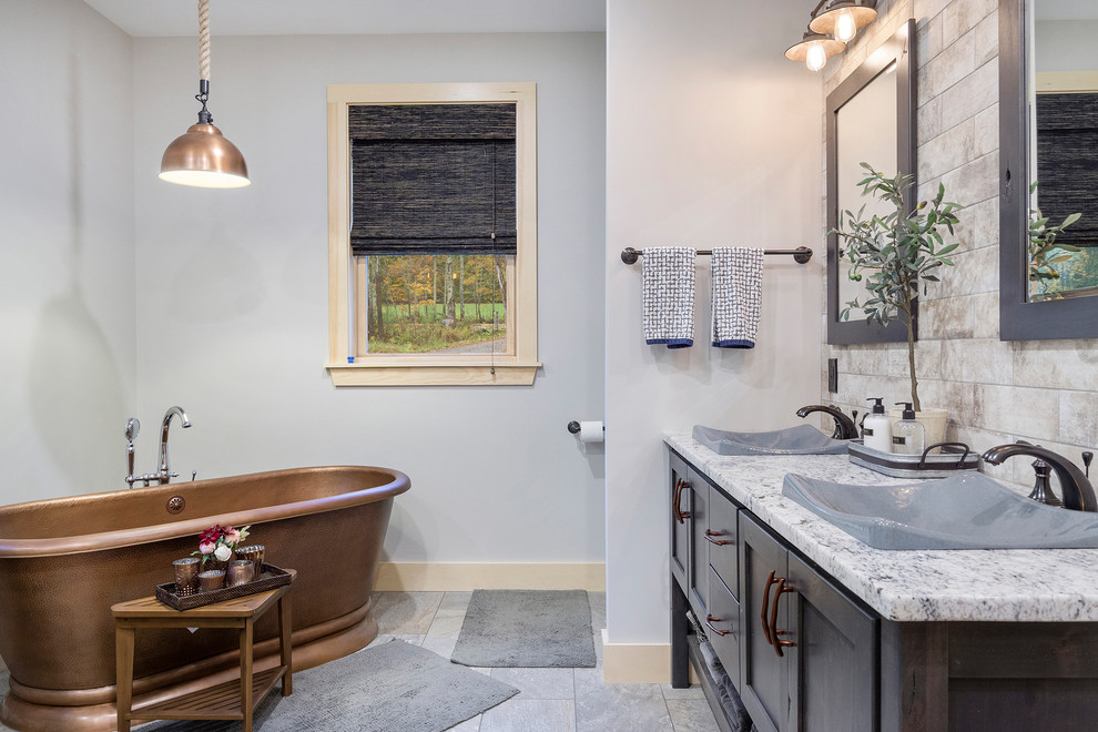 Пример оригинального дизайна: главная ванная комната в стиле рустика с темными деревянными фасадами, отдельно стоящей ванной, серыми стенами, настольной раковиной, серым полом, разноцветной столешницей, окном и фасадами в стиле шейкер