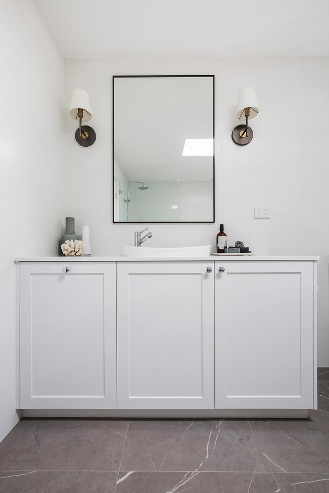This is an example of a large contemporary ensuite bathroom in Sydney with shaker cabinets, white cabinets, a freestanding bath, a walk-in shower, a wall mounted toilet, white tiles, porcelain tiles, white walls, porcelain flooring, an integrated sink, engineered stone worktops, grey floors, an open shower and white worktops.