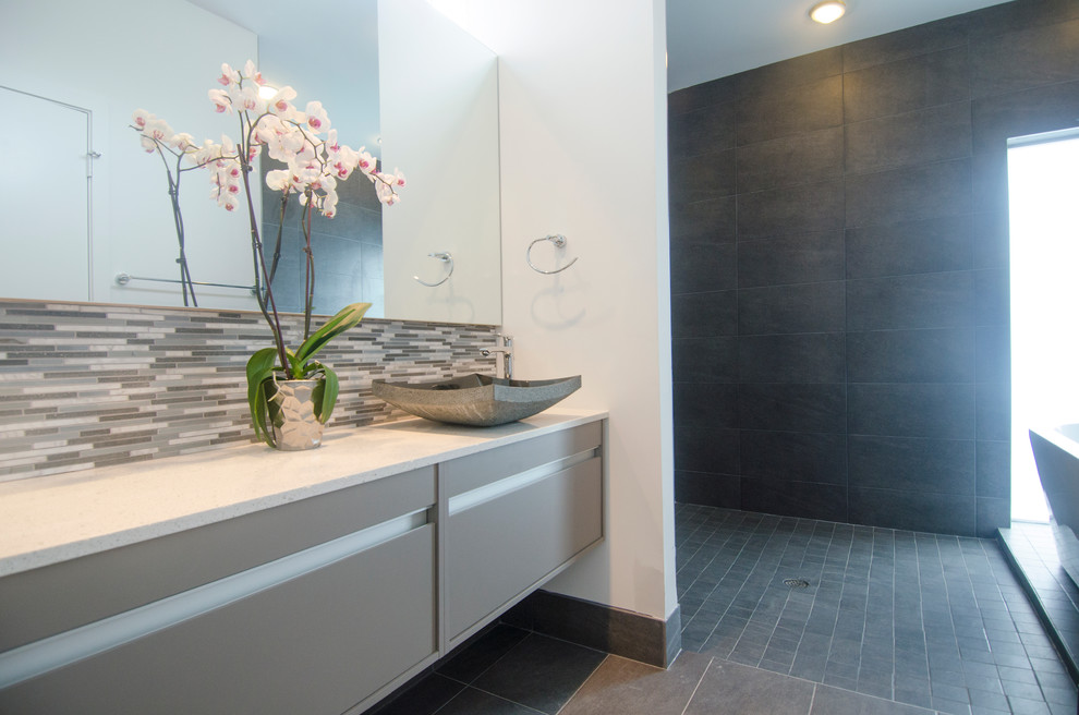 This is an example of a contemporary bathroom in Houston with a vessel sink, flat-panel cabinets, beige cabinets, engineered stone worktops, a freestanding bath, a walk-in shower, a one-piece toilet, grey tiles and porcelain tiles.