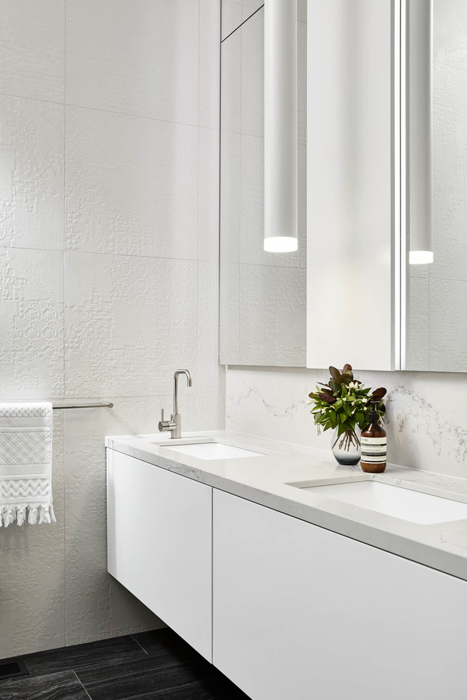 Свежая идея для дизайна: ванная комната в стиле модернизм с плоскими фасадами, белыми фасадами, белой плиткой, белыми стенами, врезной раковиной и черным полом - отличное фото интерьера