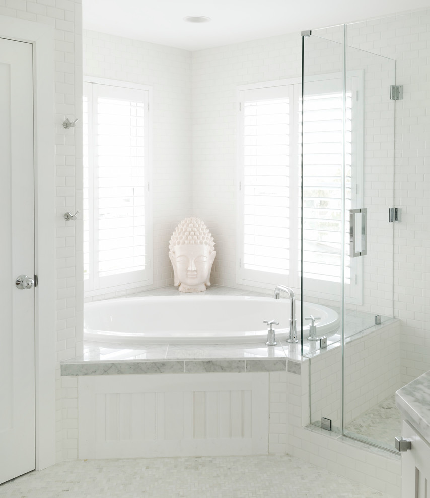 На фото: большая главная ванная комната в морском стиле с монолитной раковиной, фасадами с утопленной филенкой, белыми фасадами, мраморной столешницей, угловой ванной, белой плиткой, плиткой мозаикой и белыми стенами с