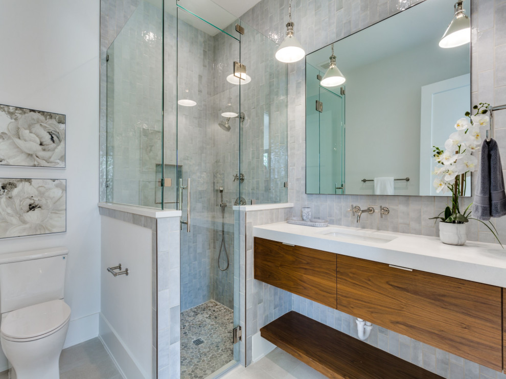 This is an example of a contemporary shower room bathroom in Dallas with flat-panel cabinets, medium wood cabinets, an alcove shower, a two-piece toilet, grey tiles, white walls, a submerged sink, engineered stone worktops, beige floors, a hinged door, white worktops, a single sink and a floating vanity unit.