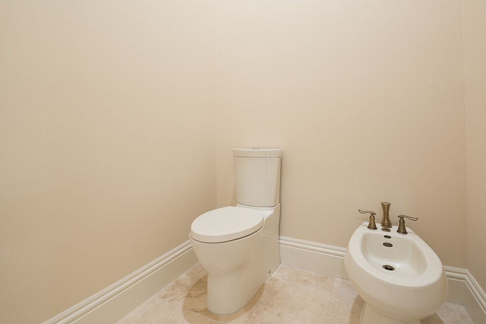 Cette image montre un très grand WC et toilettes méditerranéen avec un bidet, un carrelage en pâte de verre, un mur beige et un sol en travertin.