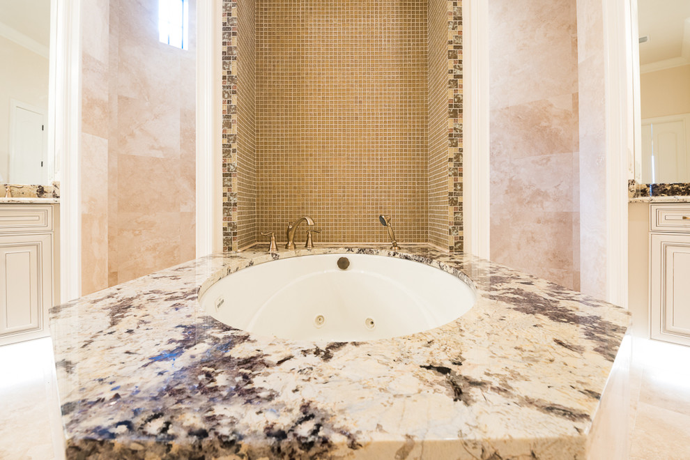 Esempio di un'ampia stanza da bagno mediterranea con ante con bugna sagomata, ante bianche, vasca sottopiano, doccia aperta, piastrelle di vetro, pareti beige, pavimento in travertino, lavabo sottopiano e top in granito