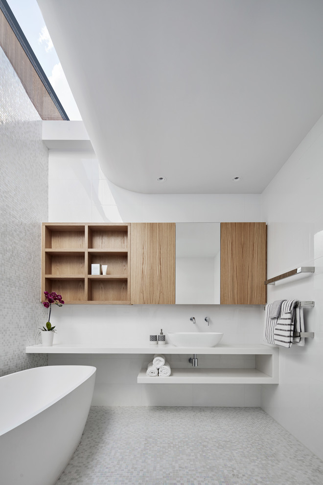 Design ideas for a medium sized contemporary bathroom in Melbourne with open cabinets, a freestanding bath, white tiles, glass tiles, mosaic tile flooring, a vessel sink, solid surface worktops, white worktops, light wood cabinets, white walls and white floors.