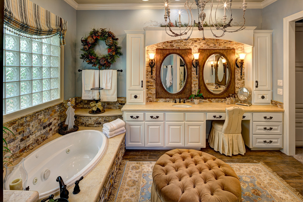 Klassisk inredning av ett badrum, med luckor med upphöjd panel, vita skåp, ett platsbyggt badkar, brun kakel, blå väggar och ett undermonterad handfat