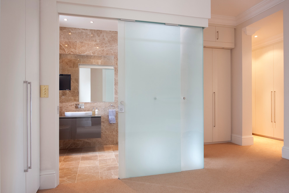 Medium sized contemporary ensuite bathroom in London with an integrated sink, flat-panel cabinets, grey cabinets, glass worktops, a double shower, a one-piece toilet, beige tiles, porcelain tiles, beige walls and porcelain flooring.