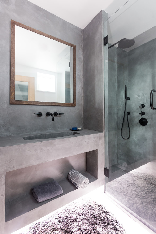 Industriell inredning av ett litet grå grått badrum med dusch, med öppna hyllor, grå skåp, en hörndusch, grå väggar, ett integrerad handfat, bänkskiva i betong, betonggolv och grått golv