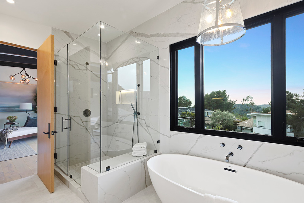 Пример оригинального дизайна: большая главная ванная комната: освещение в стиле модернизм с серой плиткой, плоскими фасадами, светлыми деревянными фасадами, отдельно стоящей ванной, открытым душем, мраморной плиткой, белыми стенами, мраморным полом, врезной раковиной, мраморной столешницей, белым полом, душем с распашными дверями, белой столешницей, тумбой под две раковины и встроенной тумбой