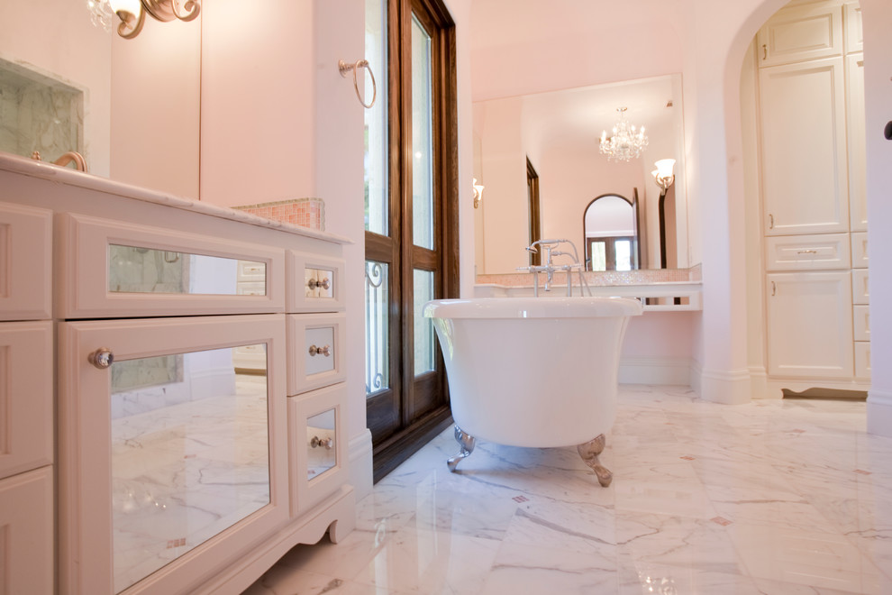 Idéer för att renovera ett mycket stort medelhavsstil badrum för barn, med ett fristående handfat, luckor med glaspanel, vita skåp, marmorbänkskiva, ett badkar med tassar, en dusch i en alkov, en toalettstol med separat cisternkåpa, vit kakel, stenkakel, rosa väggar och marmorgolv