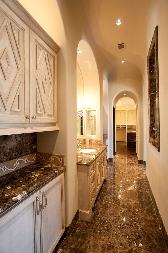 Inspiration for a huge mediterranean master brown tile and stone tile marble floor bathroom remodel in Houston with a drop-in sink, furniture-like cabinets, beige cabinets, marble countertops, a two-piece toilet and beige walls