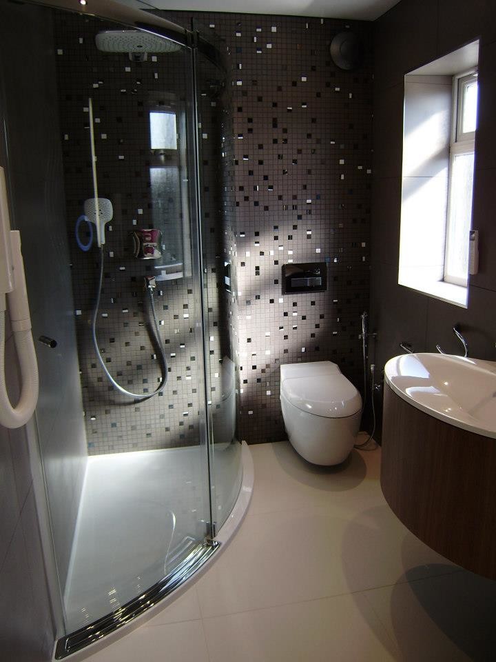 Inspiration for a medium sized contemporary shower room bathroom in West Midlands with a wall-mounted sink, flat-panel cabinets, medium wood cabinets, solid surface worktops, a double shower, a wall mounted toilet, grey tiles, porcelain tiles, grey walls and porcelain flooring.