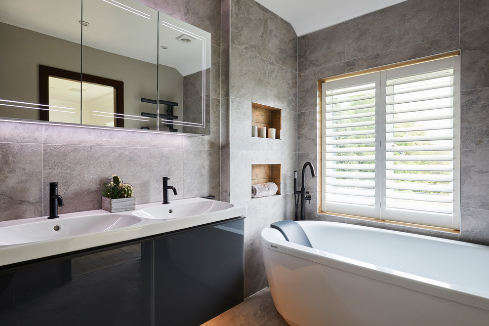 На фото: главная ванная комната среднего размера в современном стиле с плоскими фасадами, черными фасадами, отдельно стоящей ванной, серой плиткой, керамической плиткой, полом из керамогранита, серым полом и консольной раковиной с