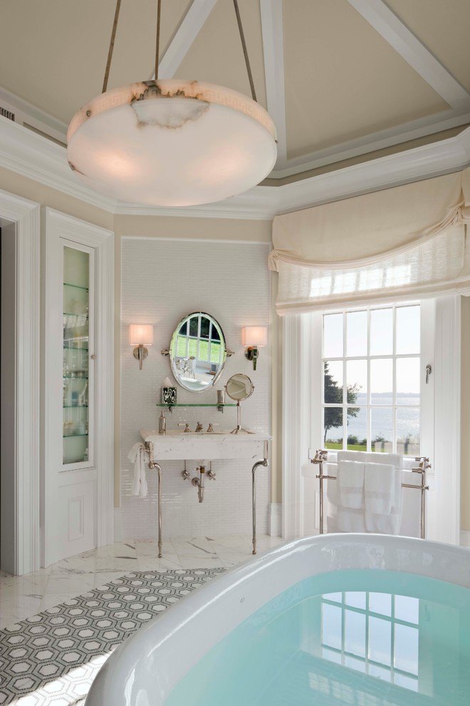 Modelo de cuarto de baño principal clásico renovado grande con bañera exenta, paredes beige, suelo de mármol, lavabo integrado, suelo blanco y encimeras beige