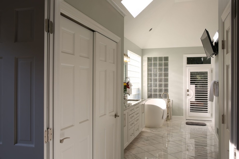 Cette image montre une salle de bain principale design de taille moyenne avec un placard à porte shaker, des portes de placard blanches, une baignoire indépendante, une douche d'angle, WC à poser, un carrelage en pâte de verre, un mur gris, un sol en marbre, un lavabo intégré, un plan de toilette en quartz modifié, un sol blanc, une cabine de douche à porte battante et un carrelage blanc.