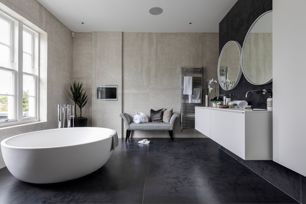 Photo of a large contemporary family bathroom in London with flat-panel cabinets, white cabinets, a freestanding bath, a walk-in shower, a one-piece toilet, black and white tiles, black walls, cement flooring, a submerged sink, solid surface worktops and black floors.